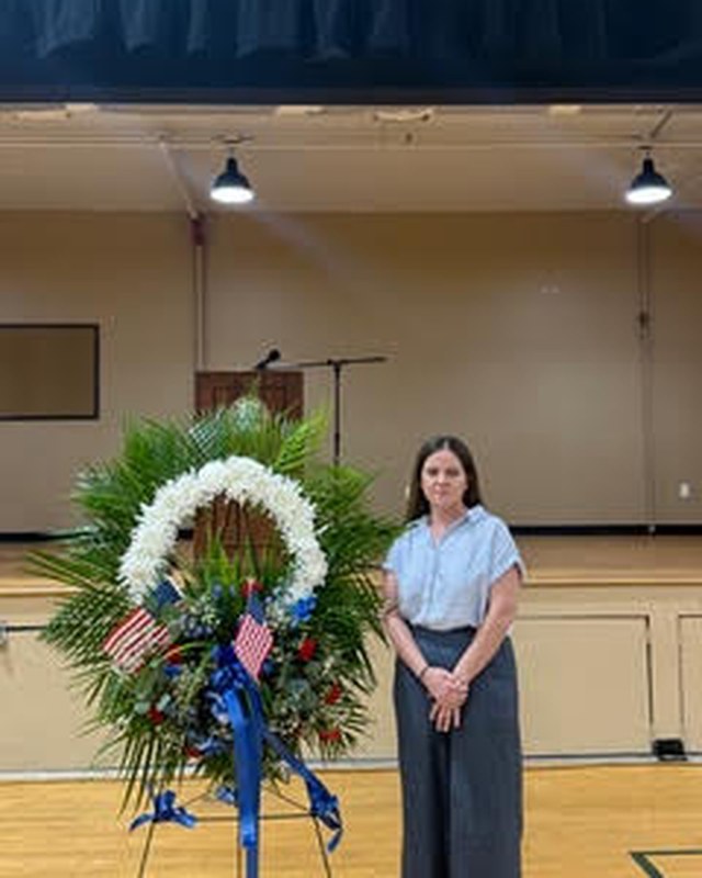 Katie standing beside a memorial wreath at a community event.